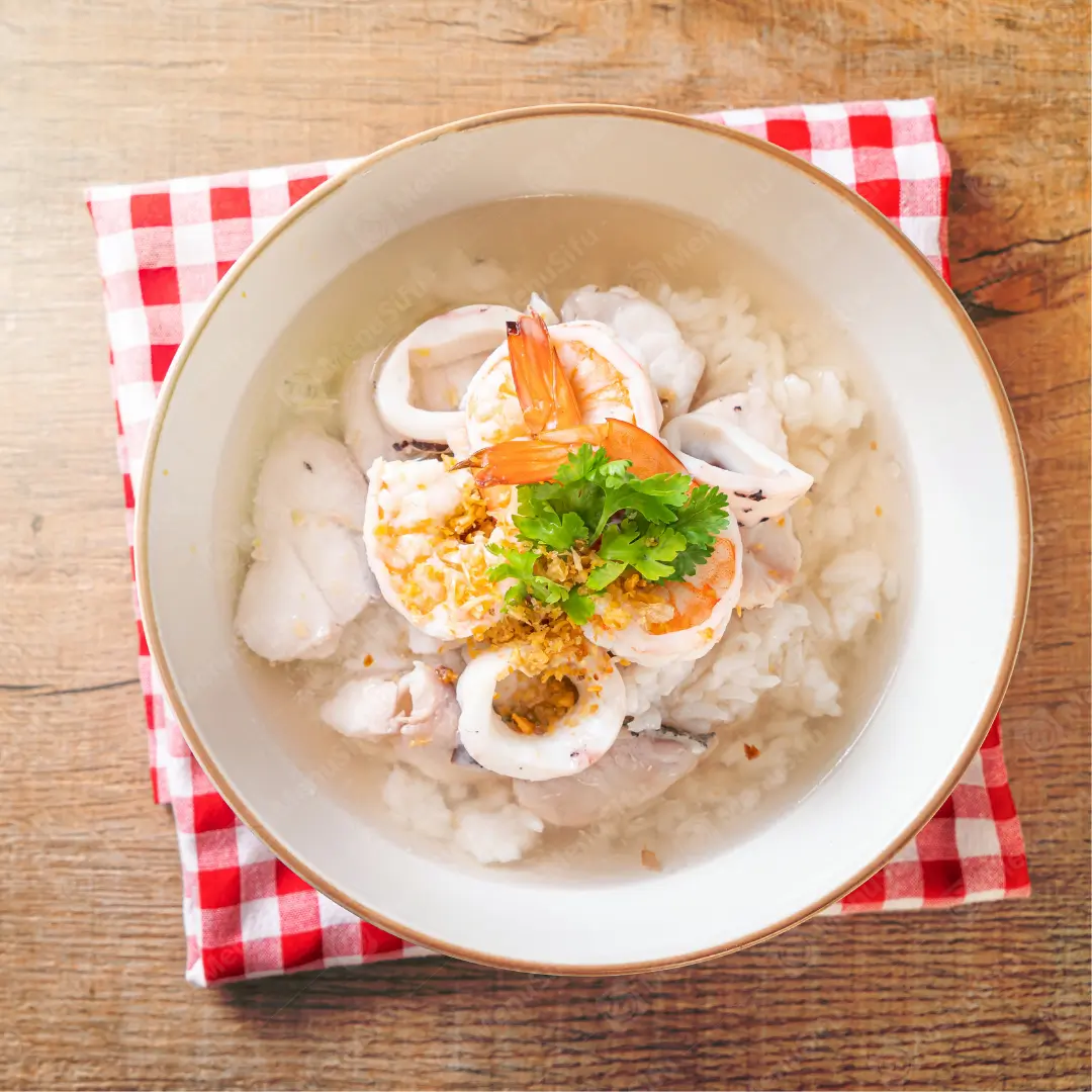 Seafood Rice Soup is a nourishing dish featuring a rice - based soup with fresh seafood like shrimp and squid, garnished with cilantro and crispy bits.
